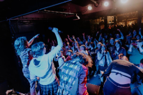 a group of musicians on stage from the back performing to an audience in low light