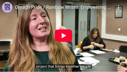 a screengrab of a video showing a woman with blonde hair speaking to camera with a group writing behind her a screengrab of a video showing a woman with blonde hair speaking to camera with a group writing behind her