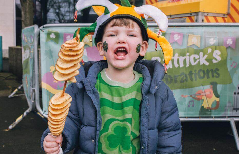 a young boy holding a potato snack at a st patricks day parade dressed in green outside