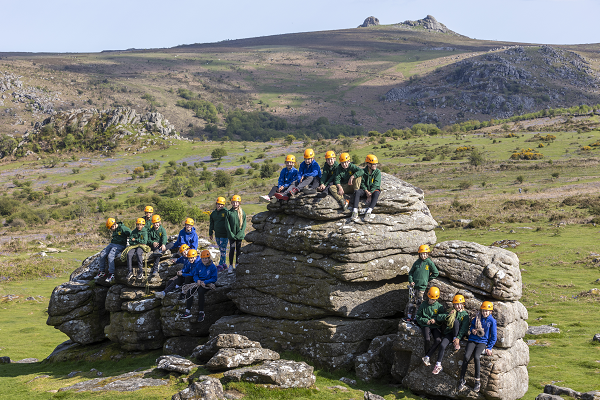 Lots of children wearing hardhats sitting on top of a series of Tors on Dartmoor