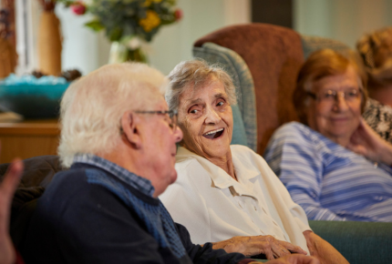 Older lady laughing and joking with a friend whilst sat on the sofa