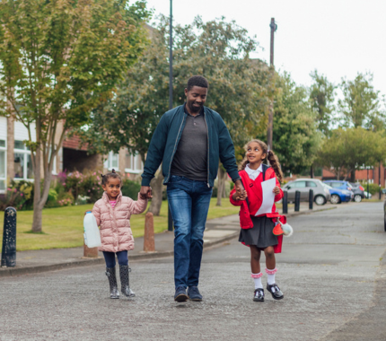 Young dad holding the hands of his two daughters either side of him as they walk to school
