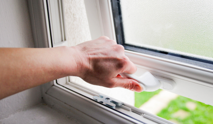 A hand is opening a window that has condensation gathered on it