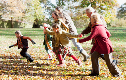 Family holding hands and laughing as they run through the autumnal leaves
