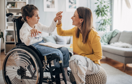 Image shows a young mum kneeling down and high fiving her son who is sat in a wheelchair