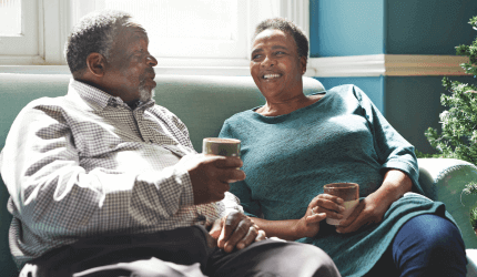 Older couple sitting on a sofa having a tea and conversing 