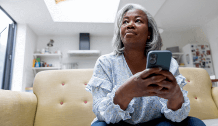 Older person sat on the sofa, holding a phone and gazing off into the distance