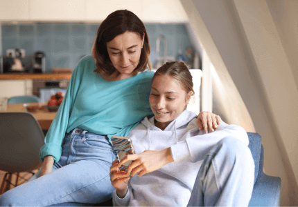 Young mum sitting with her daughter both looking at something on the daughter's phone