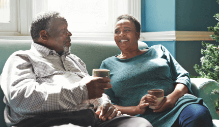 Older couple sitting on a sofa having a tea and conversing 