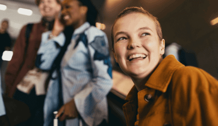 Close up of a young person with short hair smiling off into the distance with a group of friends behind her