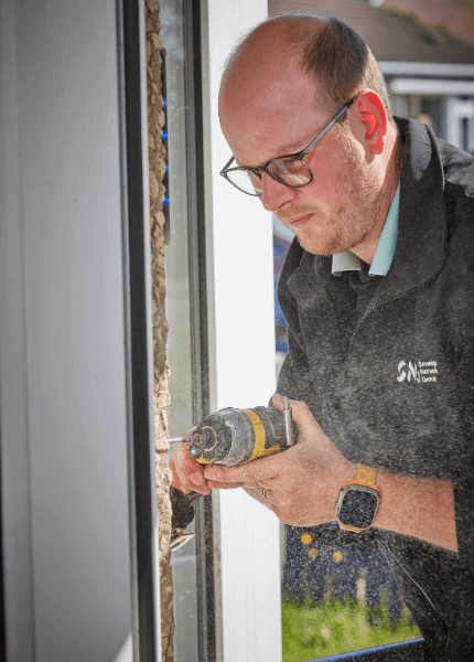 Image shows an SNG tradesperson working on a customers front door with a drill
