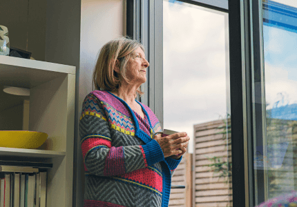 An older customer holds a cup of tea whilst looking out of the window