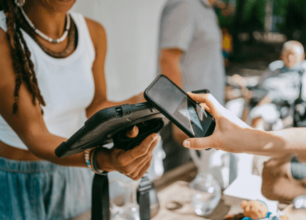 Someone pays for something using their phone whilst the store assistant holds the payment device