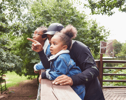 Parent stands on a wooden bridge with their two daughters looking out for birds