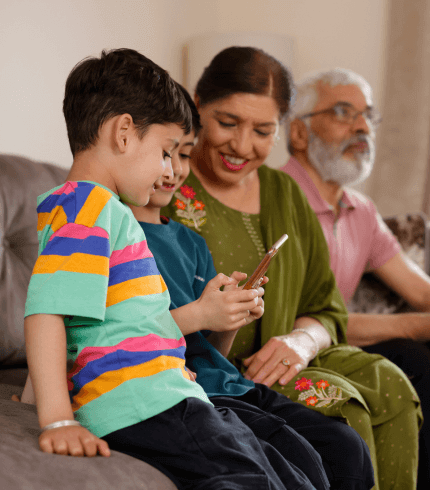Grandparents sit with their grandchildren smiling and looking at a phone