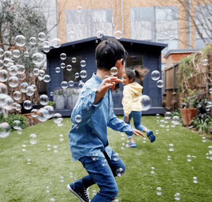 Two children run around in their back garden chasing bubbles