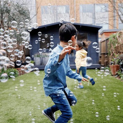 Two children run around in their back garden chasing bubbles