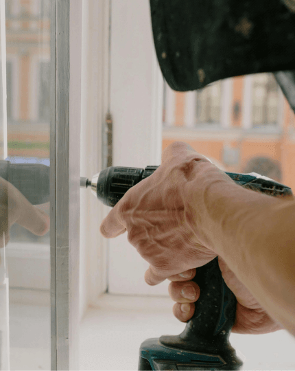 Image shows someone using an electric drill to fix a window