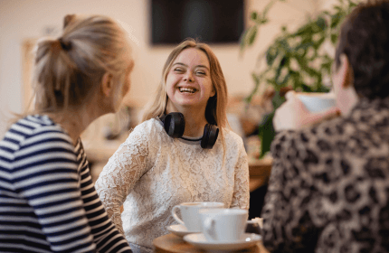Individual with downs syndrome smiles at the camera whilst enjoying a coffee with friends
