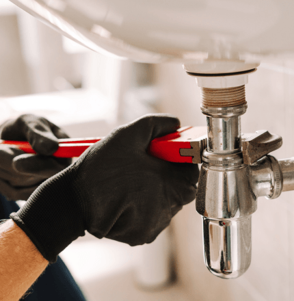 Image shows a contractor's hands using a tool to fix a leaky sink