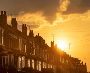 A row of terraced houses silhouetted against a golden sunset in a heatwave, with chimneys visible along the street.