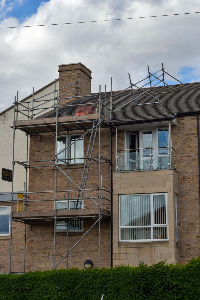 A red brick residential home with scaffolding attached to the front and roof of the property.