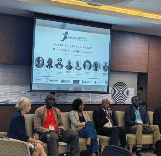 Professor Gail Davey sits on a panel at the official RESHAPE launch event in Kigali, with other speakers seated beside her and a presentation screen behind them.