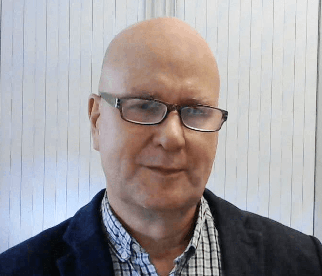 Professor Hugo Critchley wearing glasses, a dark jacket and checked shirt, photographed against a light background.