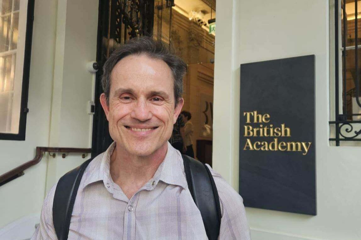 Professor Zoltán Dienes smiling outside the entrance to the British Academy, with the organisation’s sign visible beside him.