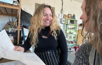 Dr Rachael Durrant smiles while looking over papers with another woman in a workshop.