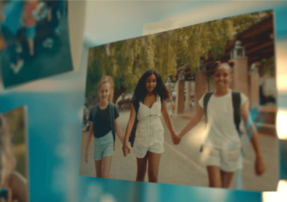 A photograph of three young people holding hands as they walk outdoors, displayed among other hanging photographs.