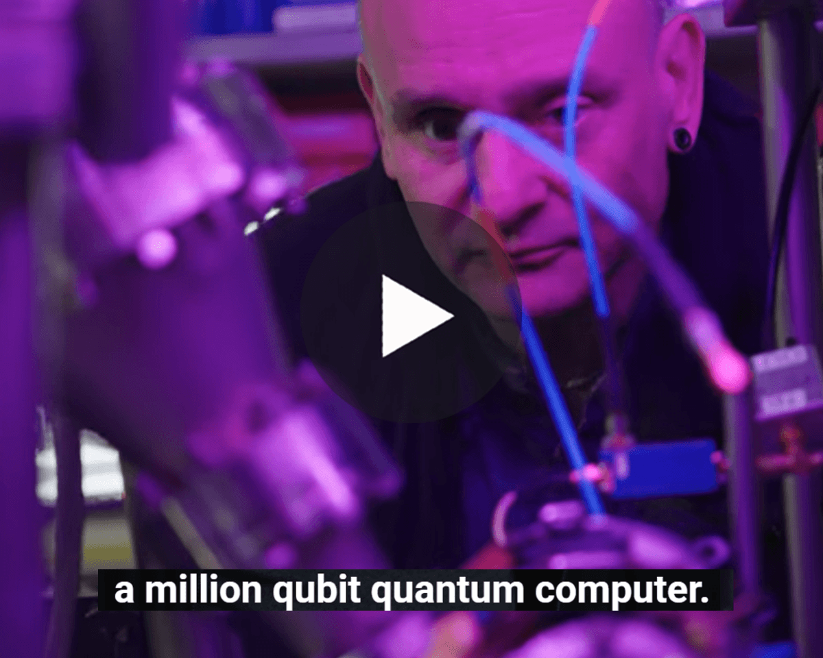 Professor Winfried Hensinger in the Sussex quantum lab, with purple-lit quantum computing equipment, a play button and the on-screen caption: “a million qubit quantum computer."