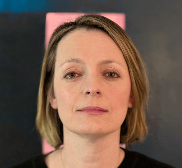 Portrait photograph of Dr Kathryn Lester against a dark background, wearing a black top and looking towards the camera.