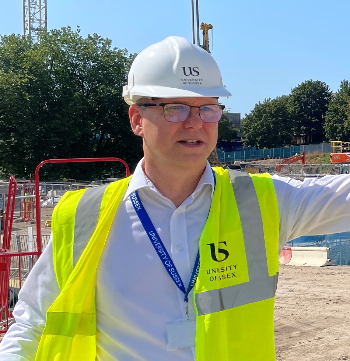 John Kallend wearing hi-vis and a University of Sussex hard hat on a construction site.