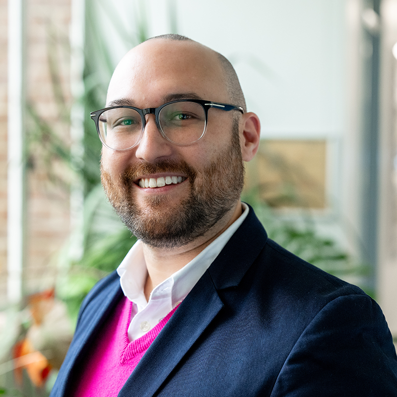 Dr Luke Yates, smiling, in a pink jumper and navy blazer.