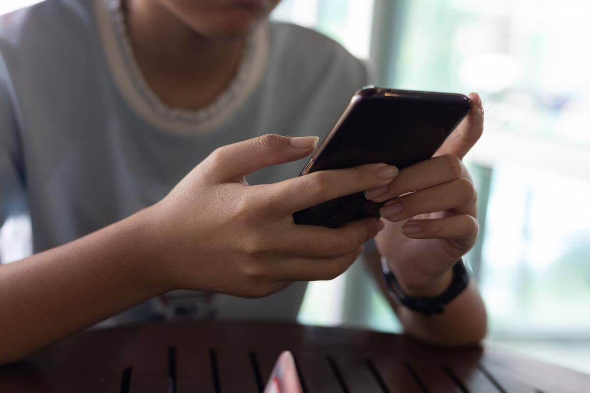 Close-up of a person holding and looking at a smartphone, seated indoors.