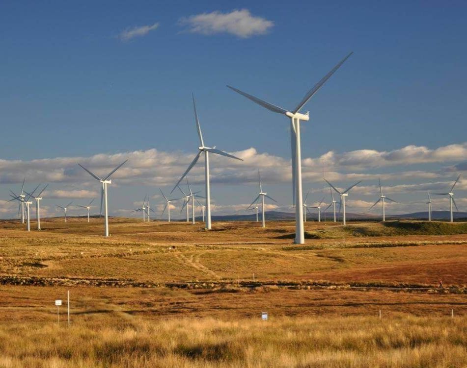 Wind turbines across open moorland under a blue sky with scattered clouds.