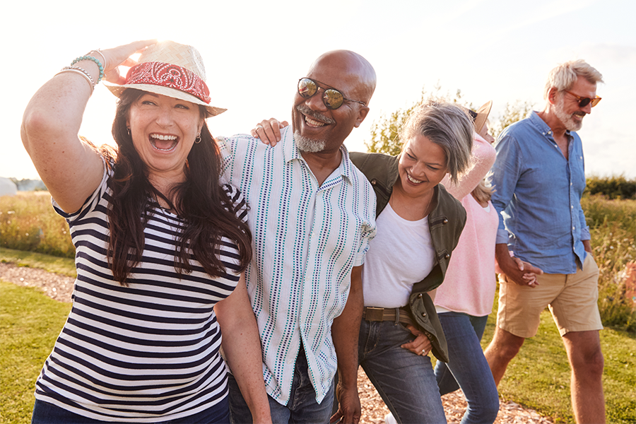Group of five middle-aged adults walking outdoors on a sunny day, laughing and smiling together.