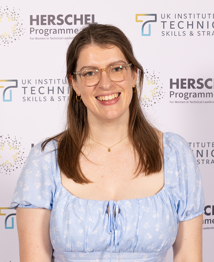 Becki Cook smiling in front of a branded backdrop for the Herschel Programme for Women in Technical Leadership and the UK Institute for Technical Skills and Strategy.